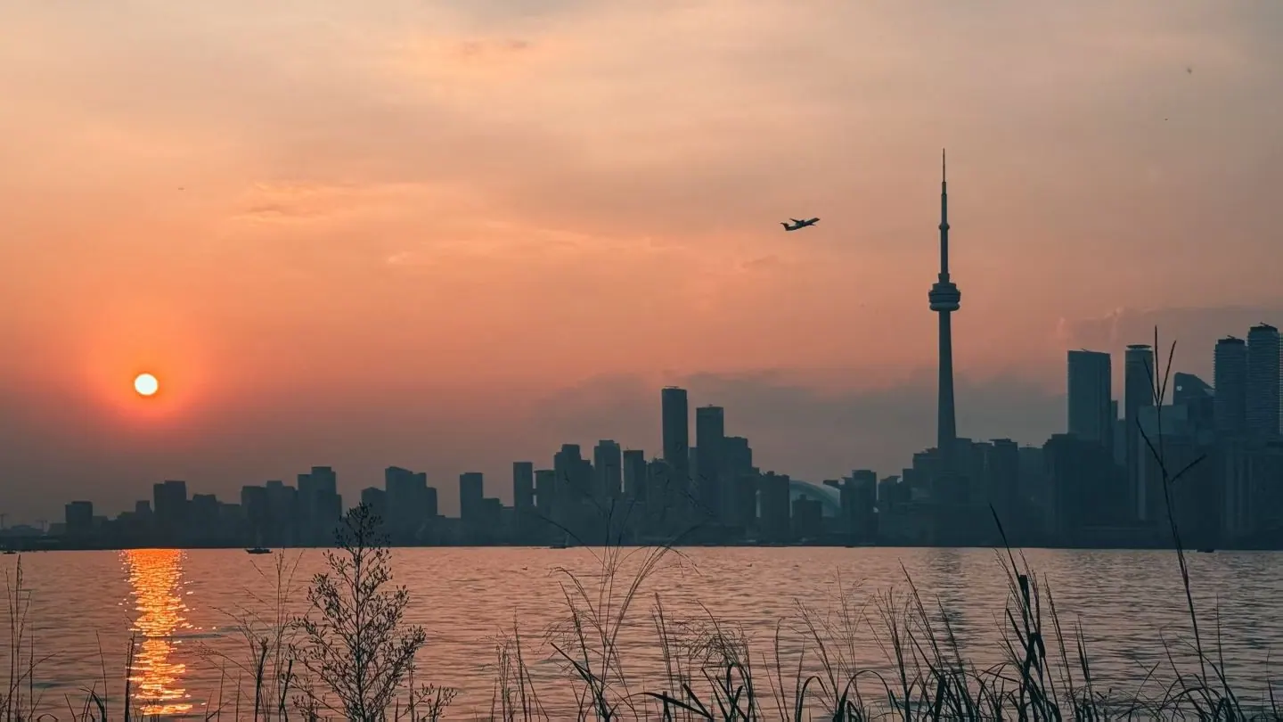 The Toronto skyline and CN Tower in silhouette at sunset, seen across Lake Ontario.